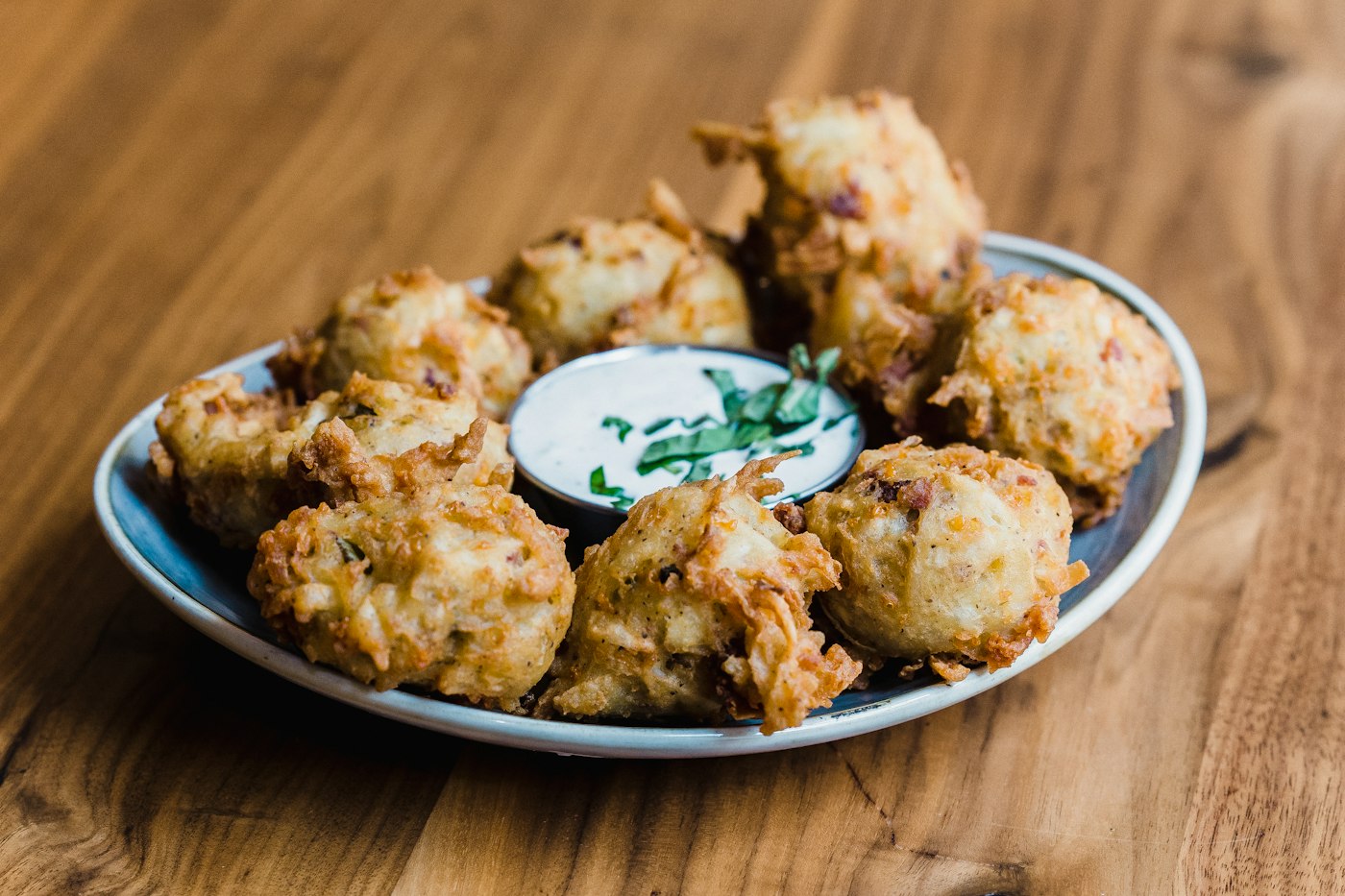 Golden vegetable fritters with a small bowl of herb dip on a wooden board