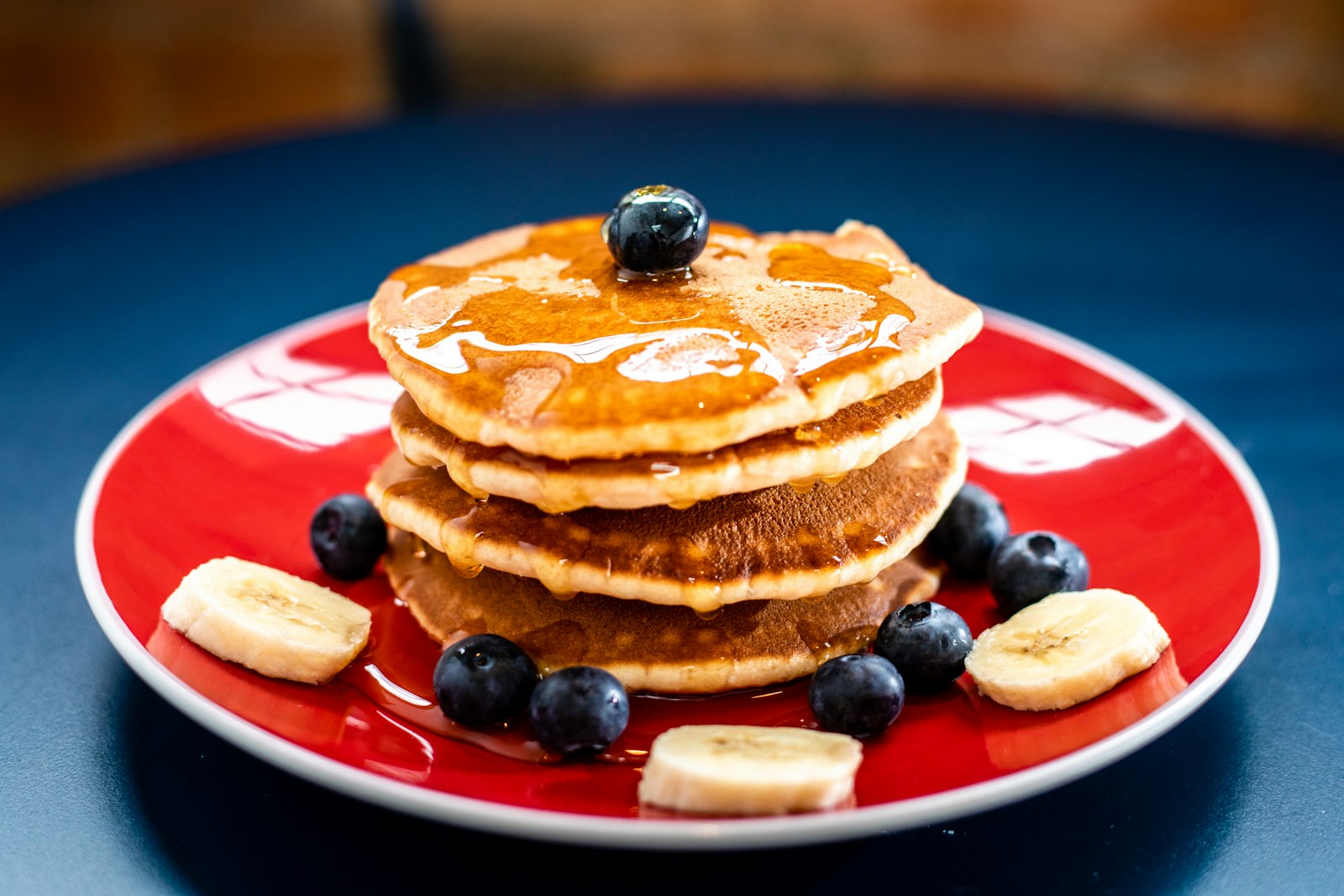 A stack of banana pancakes with blueberries on a bright red plate